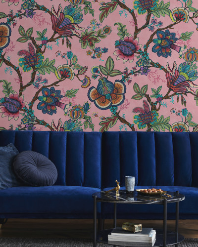 Tapet cu model floral vibrant, in nuante de roz, cu flori colorate si frunze verzi, decorat cu un canapea bleumarin, o masuta de cafea si o planta in ghiveci.