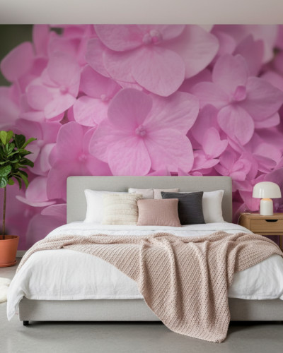 Fototapet Pink Petal Whisper personalizat cu petale mari de hortensie roz pe peretele unui dormitor modern. Pat dublu gri cu așternuturi albe și pătura roz, noptieră din lemn și plantă verde.