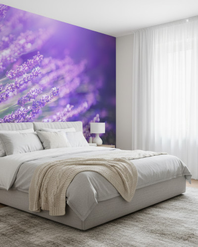 Fototapet personalizat Provence Lavender Dream cu câmpuri luxuriante de lavandă violet pe peretele principal al unui dormitor modern. Patul este gri, cu lenjerie albă și pătură bej împletită. Există o noptieră din lemn cu lampă albă și o plantă mică, și o