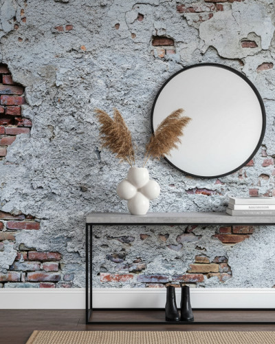 Fototapet personalizat Heritage Brick Patina, reprezentând un perete cu zidărie veche expusă și tencuială gri deteriorată, într-un decor interior cu oglindă rotundă și masă consolă.