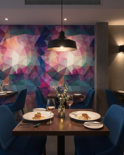 Fototapet geometric multicolor cu fațete unghiulare vibrante, decorând peretele unui restaurant modern cu scaune albastre și mese aranjate.