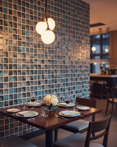 Tapet mozaic cu efect de cioburi de sticlă în nuanțe de albastru și turcoaz, într-un restaurant modern, cu mese aranjate și lumini calde.