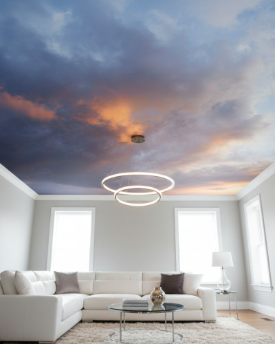 Fototapet personalizat cu cer noros la apus, instalat pe tavanul unui living modern, cu o canapea albă în formă de L, masă de cafea rotundă și un corp de iluminat suspendat circular.