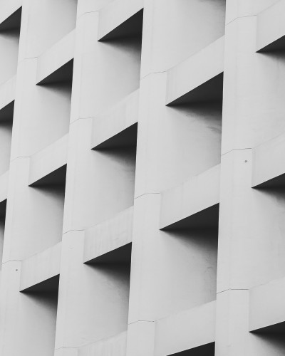 Tapet fototapet cu model geometric 3D, monocrom, pe peretele unui living modern, cu canapea gri, măsuță de cafea din lemn și decor minimalist.