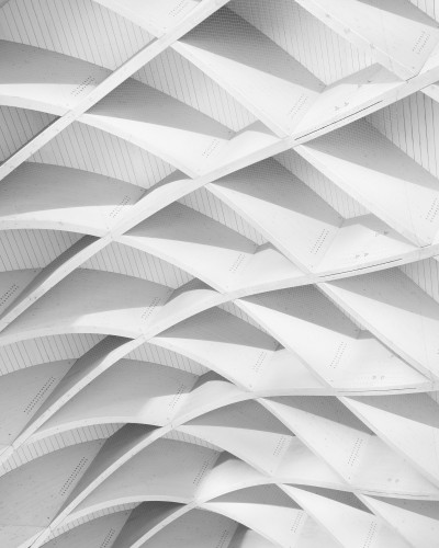 Fototapet modern Lineage Unveiled personalizat, cu model geometric 3D abstract în nuanțe de gri, aplicat pe peretele unui living minimalist cu canapea crem și mobilier contemporan.