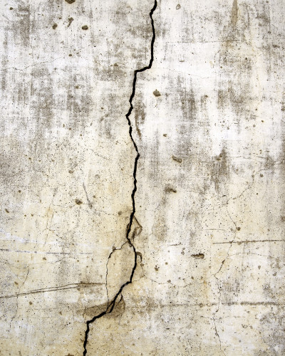 Fototapet personalizat Urban Fracture Wall cu efect de beton degradat și fisură, montat într-un living modern cu canapea gri, măsuțe de cafea și lampadar negru.