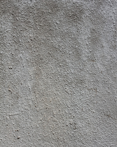 Tapet personalizat Urban Grit cu textură de beton gri pe peretele accent al unui living modern, cu canapea bej, masă rotundă din lemn și plante verzi.