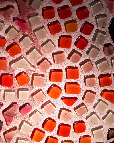 Fototapet personalizat Stained Glass Shards, cu model mozaic de sticlă colorată în nuanțe de roșu, portocaliu și alb, iluminat din spate, decorând peretele unui restaurant elegant cu mese aranjate.