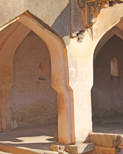 Fototapet personalizat Hampi Vaulted Splendor, înfățișând arcade boltite antice și ziduri texturate într-un living modern cu o canapea verde, masă de cafea și plante, creând o atmosferă caldă și istorică.