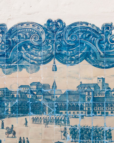 Fototapet Lisbon Tile Story cu model Azulejo albastru și alb, reprezentând un peisaj urban istoric, montat într-un living modern cu canapea bej și plante verzi.