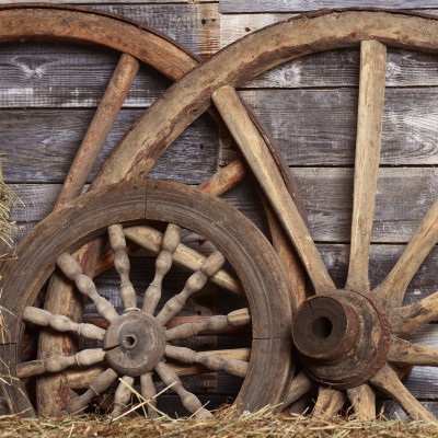 Fototapet Rustic Cartwheel Patina - personalizat, într-un restaurant modern cu scaune verzi, având un perete decorat cu roți de căruță vechi și baloturi de fân, creând o atmosferă caldă și primitoare.