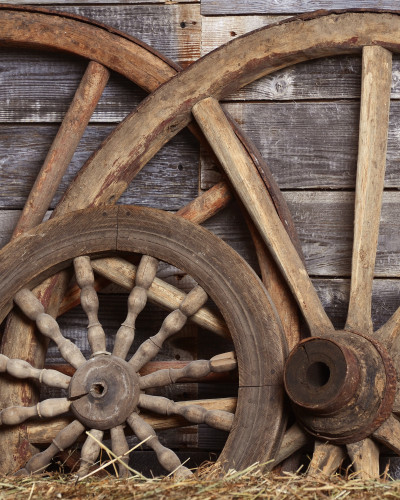 Fototapet Rustic Cartwheel Patina - personalizat, într-un restaurant modern cu scaune verzi, având un perete decorat cu roți de căruță vechi și baloturi de fân, creând o atmosferă caldă și primitoare.