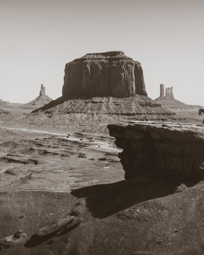 Fototapet personalizat Red Rock Vista, cu un peisaj deșertic vast, formațiuni stâncoase iconice și un cowboy călare, în tonuri sepia. Instalat într-un restaurant modern.